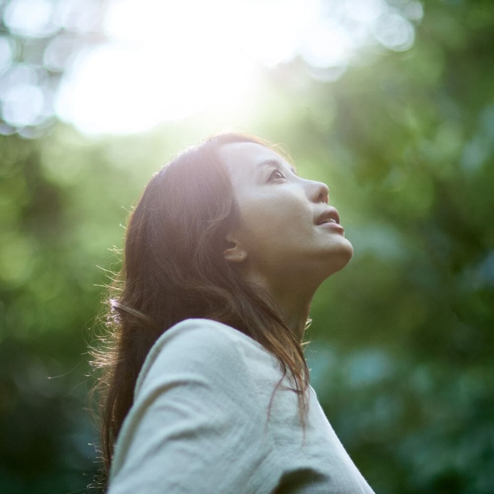 Woman looking upward in sunlit forest
