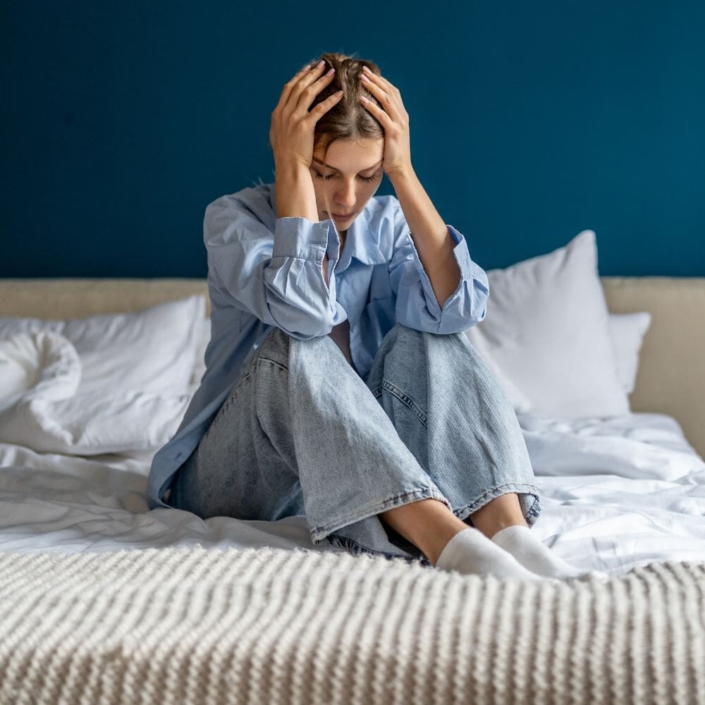 Woman on bed holding head in distress