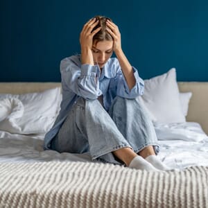 Woman on bed holding head in distress