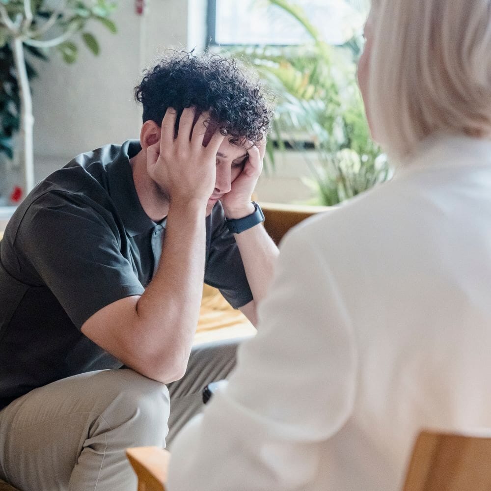 A distressed man sits with his head in his hands during a therapy session