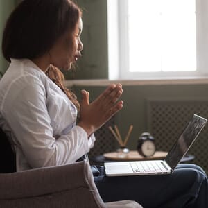 A female therapist in a white coat conducts an online therapy session