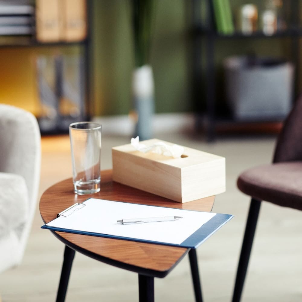 A cozy therapy office setup with a clipboard, pen, tissue box, and glass of water