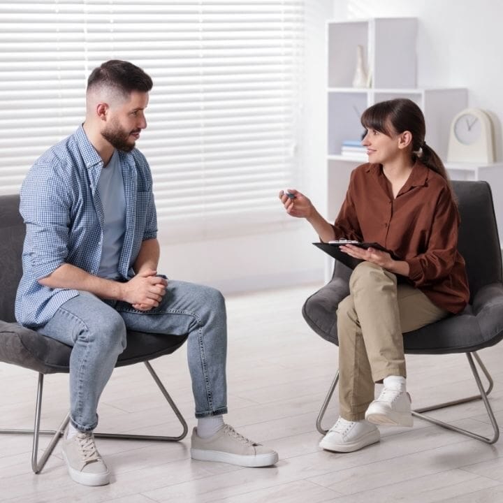 A therapist speaks with a male client during a structured trauma-processing session.