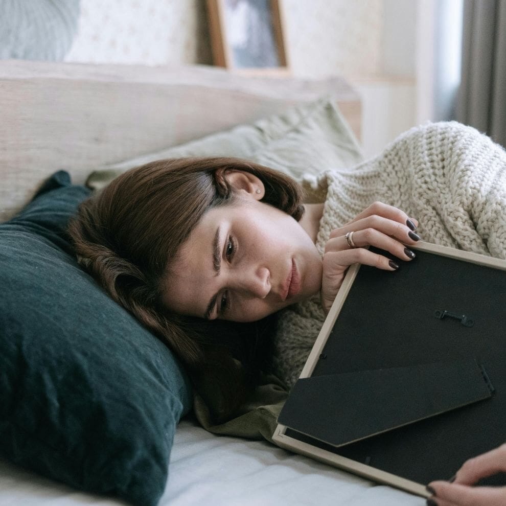 Woman lying on bed holding a picture frame and reflecting on painful memories.