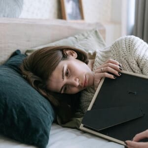 Woman lying on bed holding a picture frame and reflecting on painful memories.