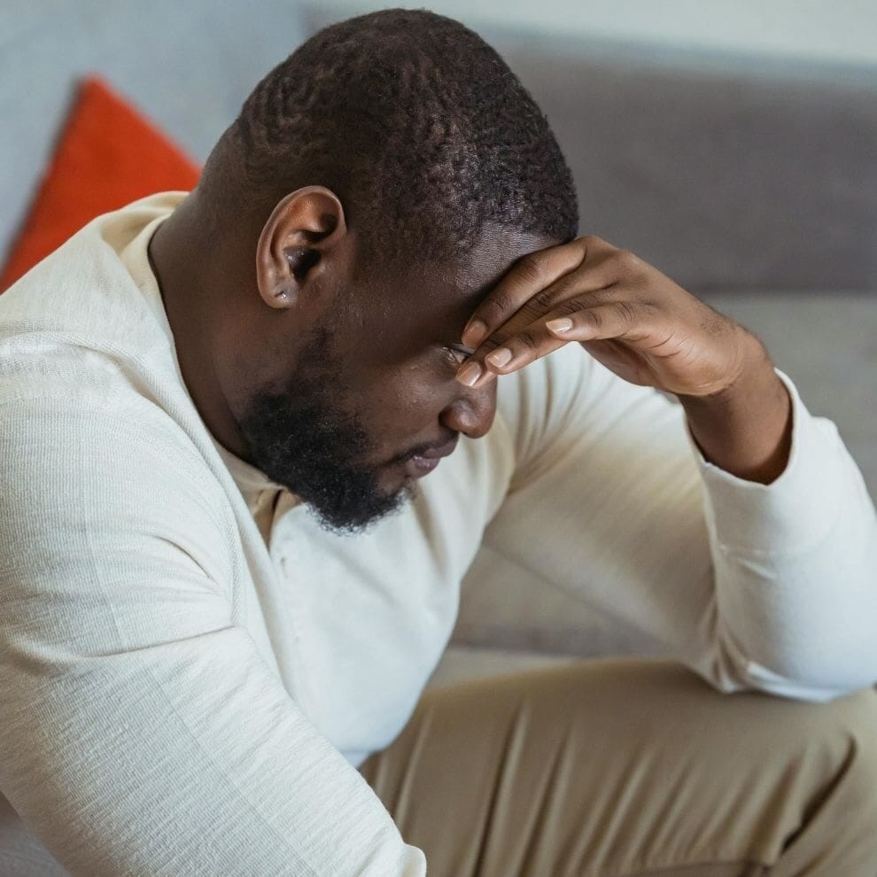 Man sitting with head in hand showing signs of emotional stress.